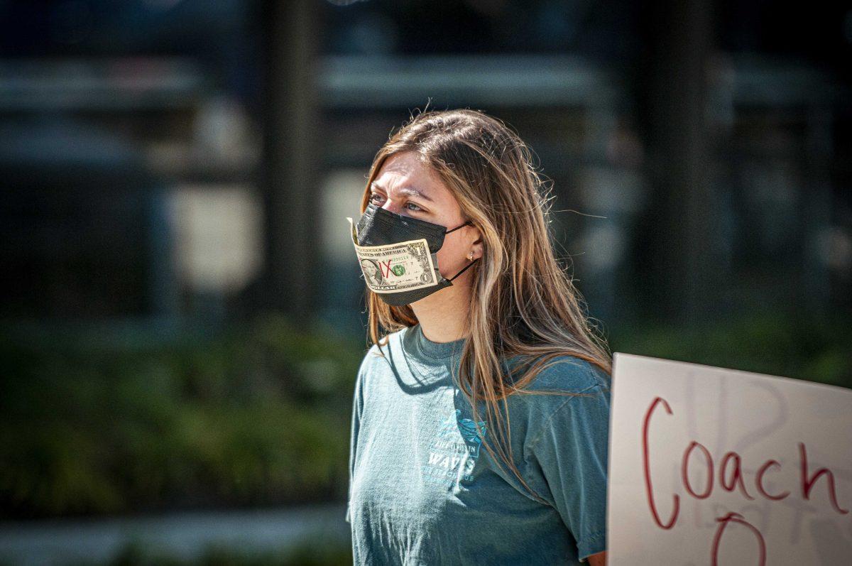 Mass communication sophomore Carley Oakley wears a mask with a dollar bill covered in "Title IX" on Monday, March 8, 2021 during the Tigers Against Sexual Assault sit-in at the Football Operations Center on Skip Bertman Drive.