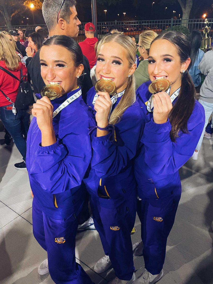 Samantha Colombi, Aubree Lavergne, Chloe Tourelle take a bit out of their gold medals at the National Championship in Orlando.