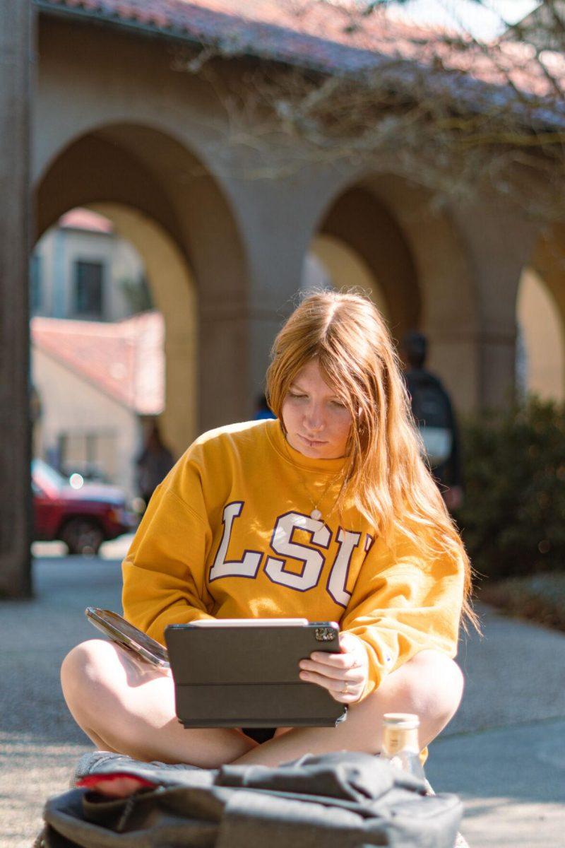 LSU sophomore English major Mary Claire Pittman works on her tablet on Tuesday, Feb. 15, 2022, while sporting a yellow LSU sweatshirt in the LSU Quad in Baton Rouge, La.