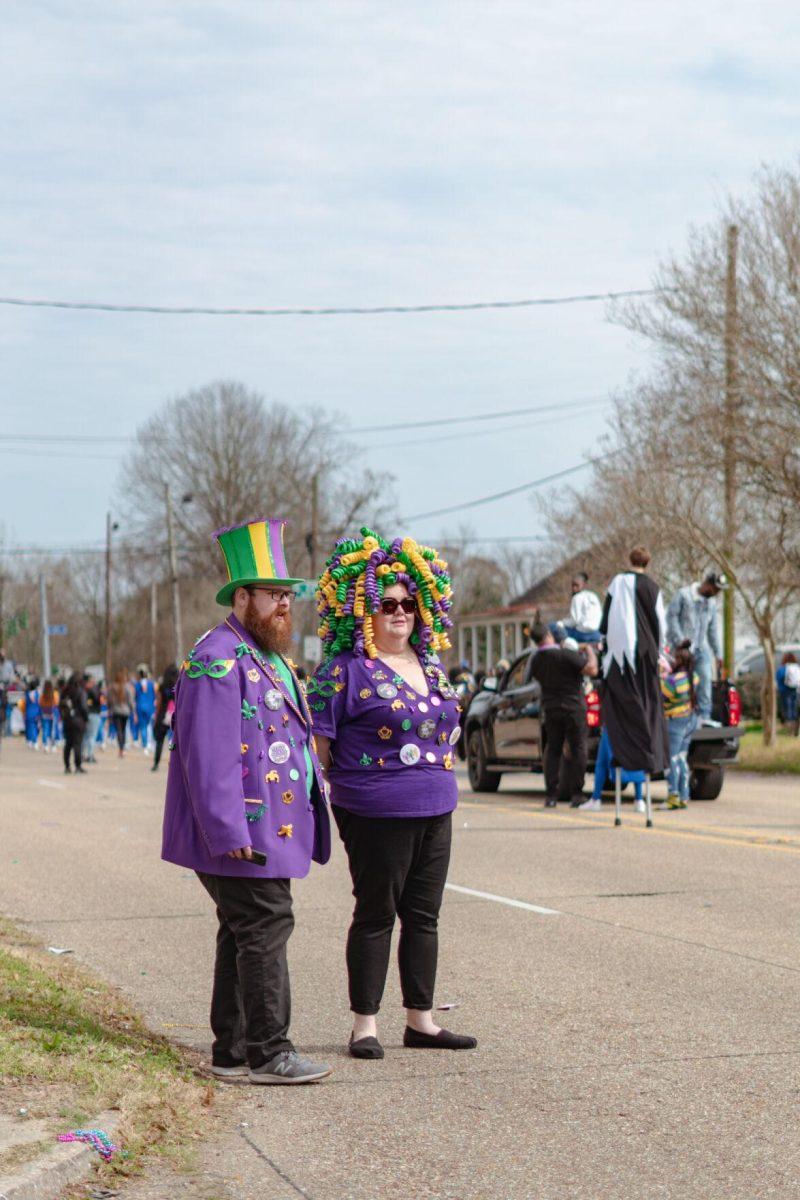 A pair decked out in Mardi Gras attire stands in the street on Sunday, Feb. 20, 2022, watching as the Mid City Gras parade goes by on North Boulevard in Baton Rouge, La.