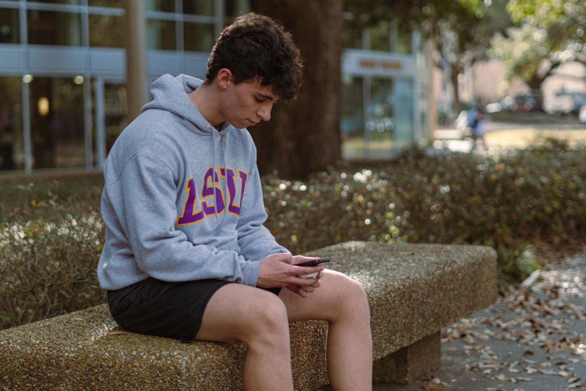 LSU architecture freshman Aidan Champagne looks at his phone on Tuesday, Feb. 22, 2022, while wearing an LSU sweatshirt in front of the LSU Student Union on Highland Road in Baton Rouge, La.