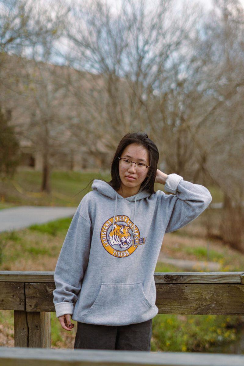 LSU senior architecture major Victoria Cheung fixes her hair on Thursday, Feb. 24, 2022, while wearing a grey LSU sweatshirt on the bridge by the Business Education Complex on South Quad Drive in Baton Rouge, La.