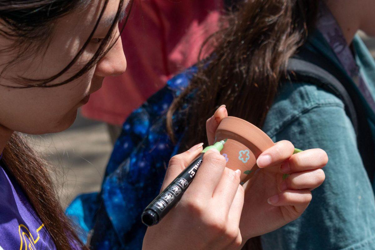 A student decorates a small clay pot using a paint pen.