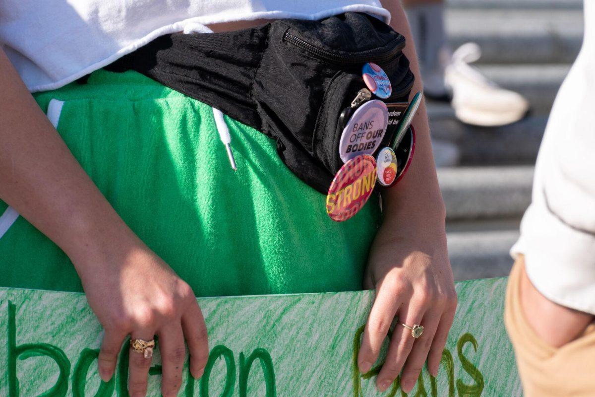 A student holds a sign and displays activism pins on her fanny pack.