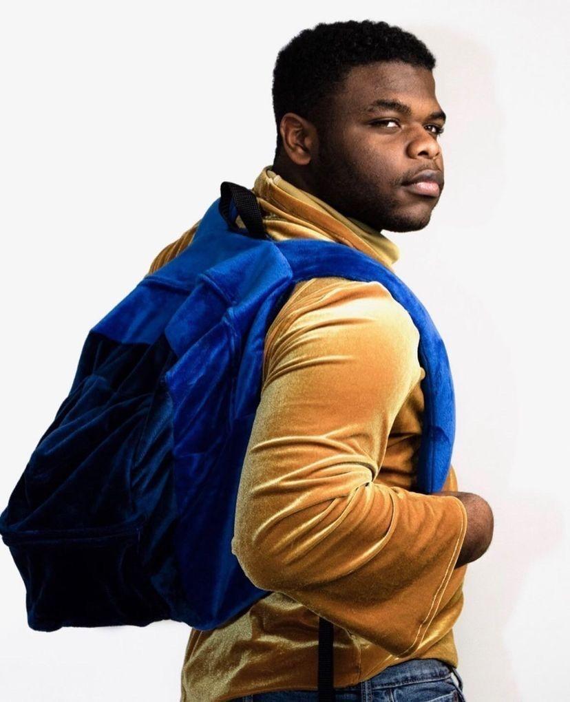 Kaleb Duncan poses with a sweater and backpack he designed.