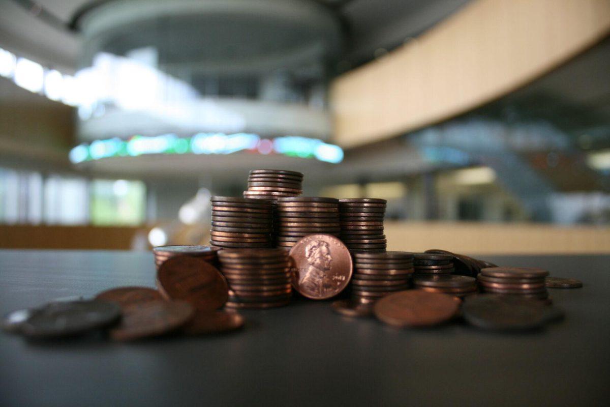 A pile of pennies collectively valued around $1.50 sits in front of the Business Education Complex's stock ticker on Friday, July 1, 2022.