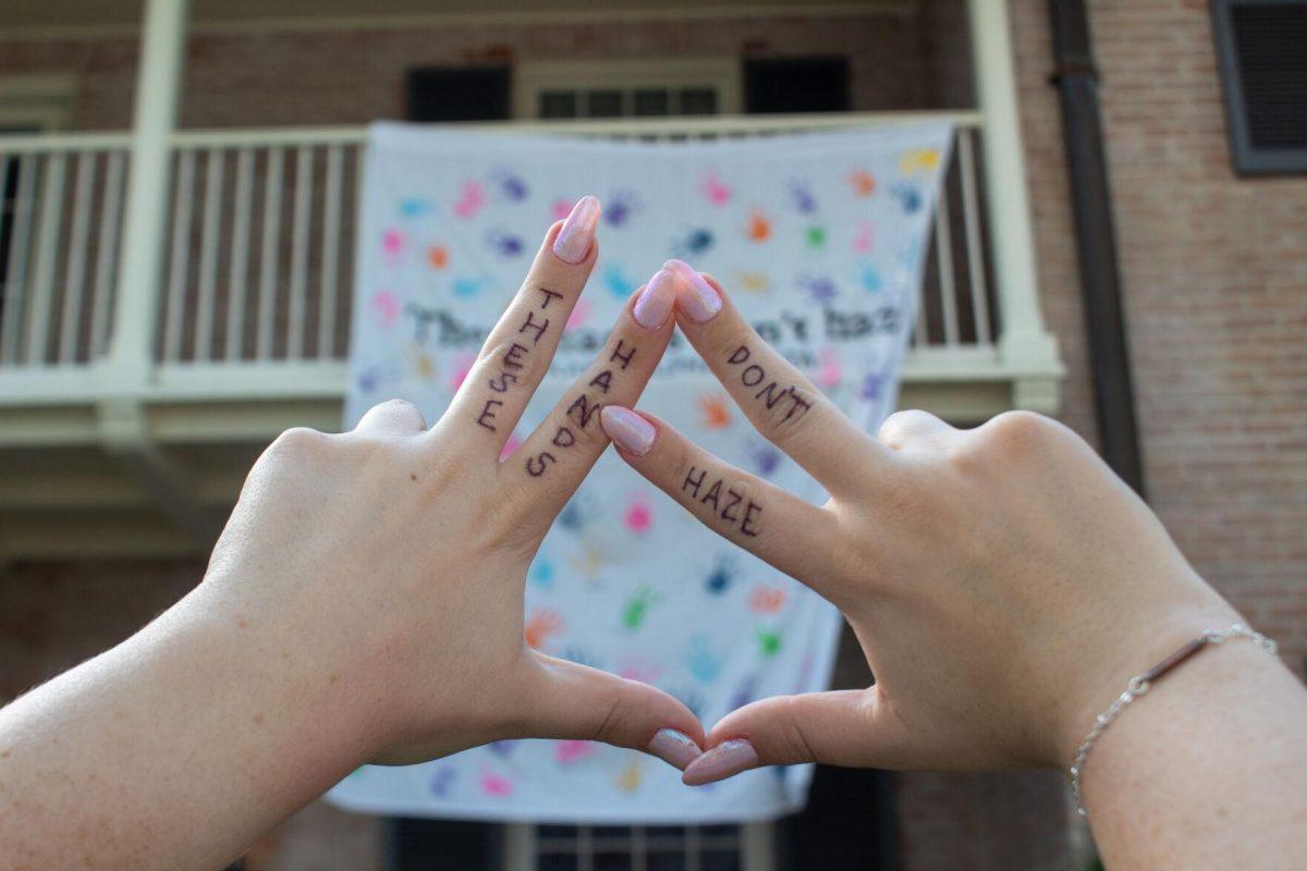 Junior LSU student Laine Cohen's hands hold up sorority hand sign in front of hazing prevention banner on Thursday, Sept. 22, 2022 on W Lakeshore Drive in Baton Rouge.