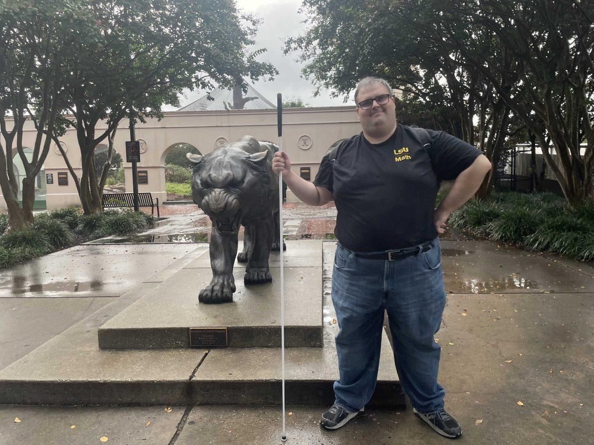 Partially blind math graduate student Justin Champagne holds his cane next a statue of Mike the Tiger on September 16, 2022.