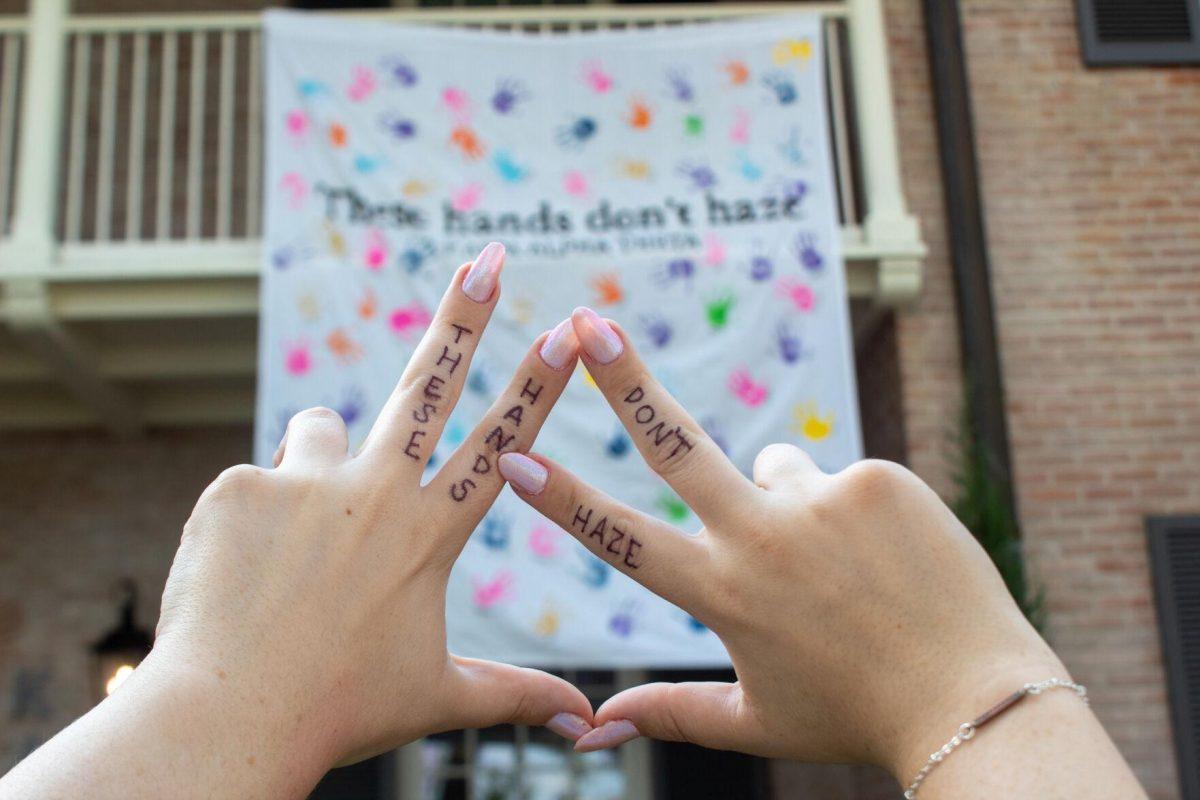 Junior LSU student Laine Cohen's hands hold up sorority hand sign in front of hazing prevention banner on Thursday, Sept. 22, 2022 on W Lakeshore Drive in Baton Rouge.