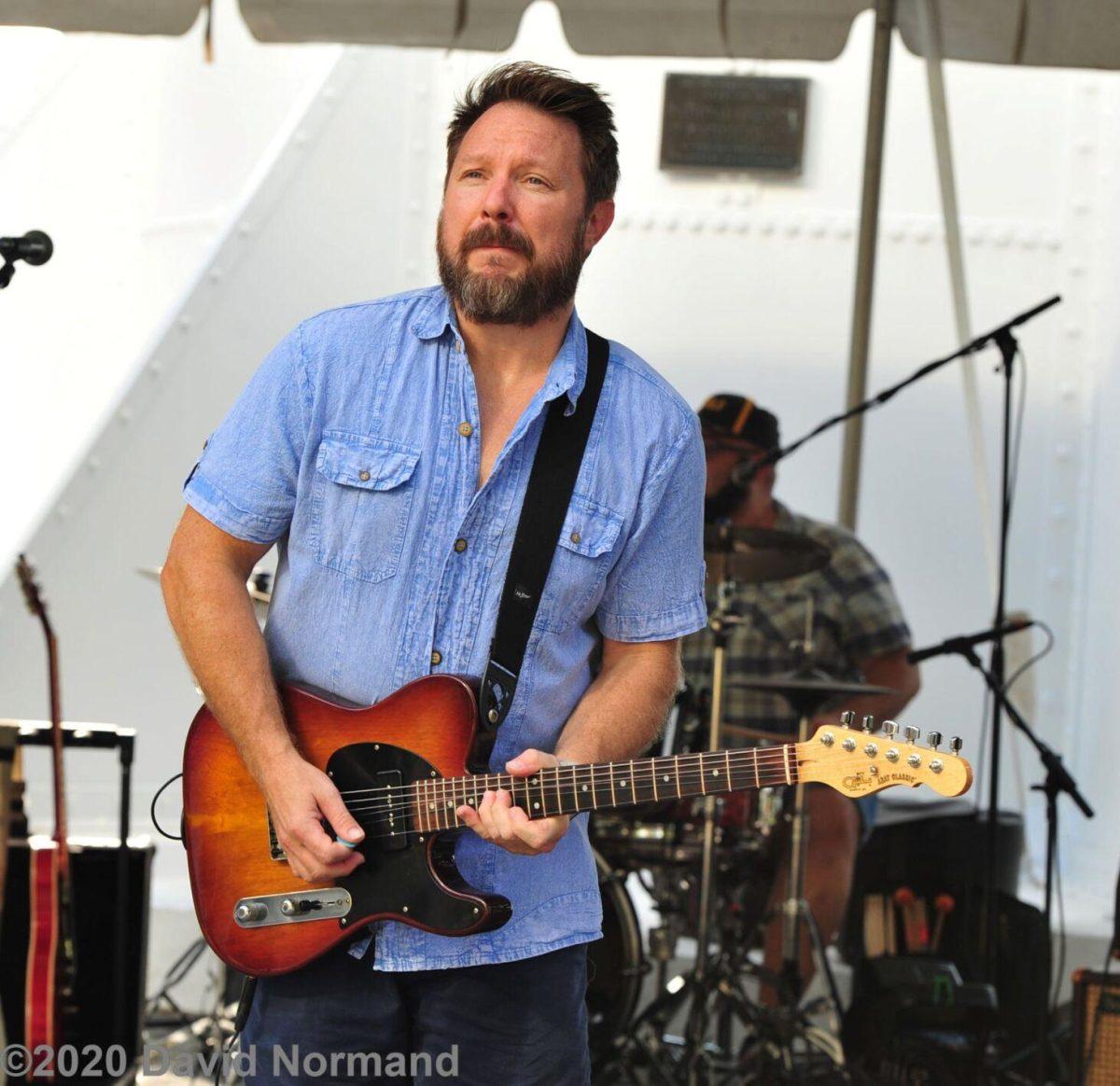 Cam Pyle strums out a tune on his guitar with a turquoise blue pick.