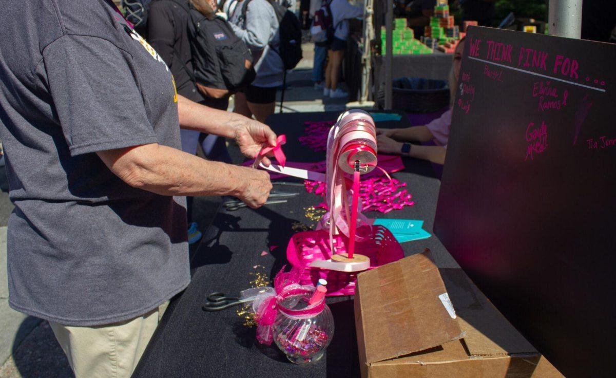 A woman cuts a pink ribbon at the Zeta Tau Alpha booth in honor of breast cancer awareness month on Wednesday, Oct. 5, 2022, on Tower Drive in Baton Rouge, La.