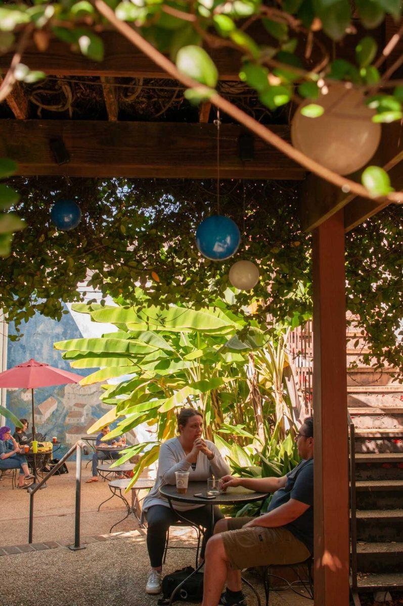 A man and a woman chat under the shade of a building and overgrown ivy&#160;on Saturday, Oct. 1, 2022,&#160;at Highland Coffees on Highland Road in Baton Rouge, La.