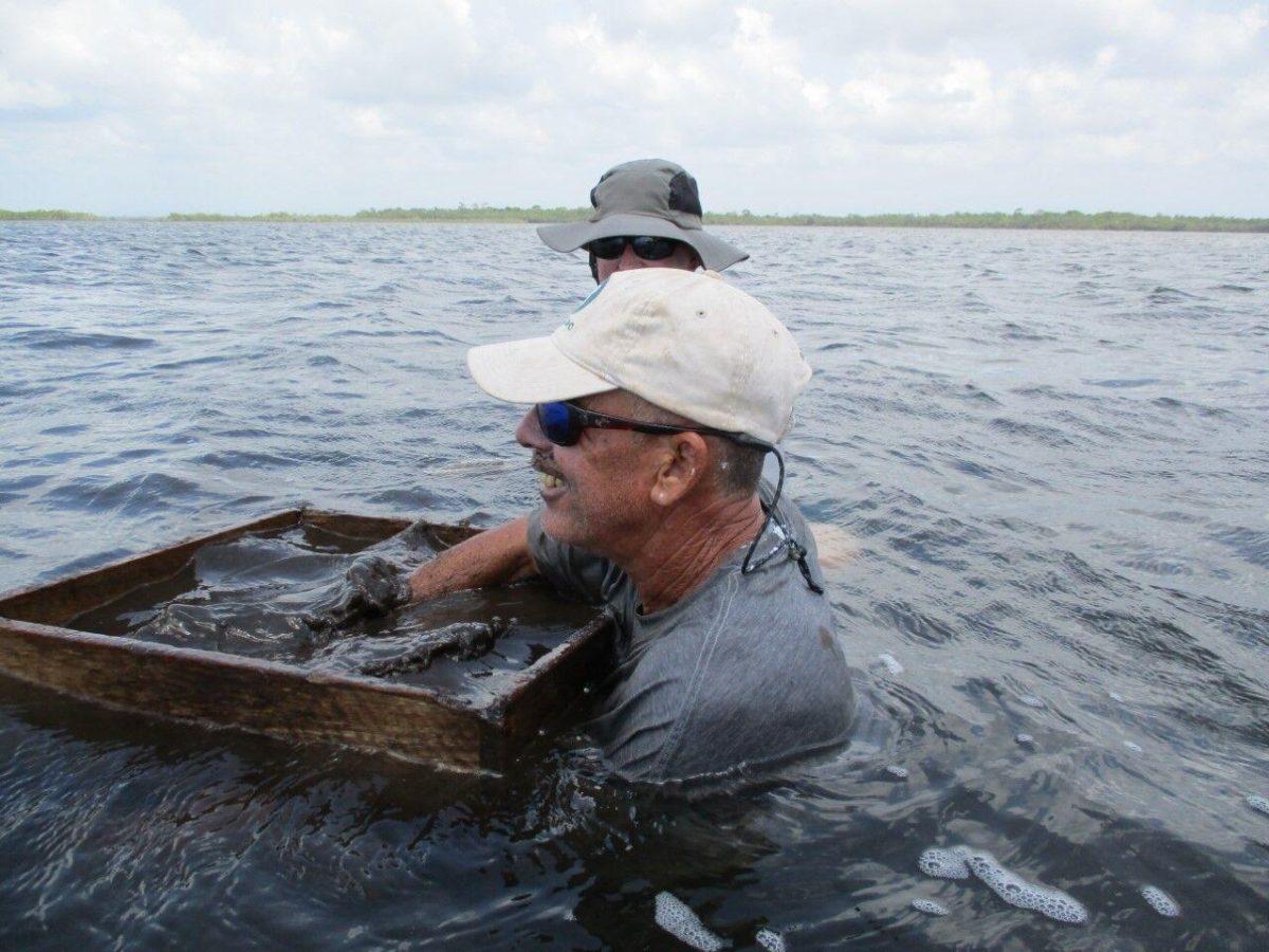 John Young, boat driver and member of the field team at Ta&#8217;ab Nuk Na, washing sediment from excavations in a box screen with mesh on the bottom to find artifacts, with Cher Foster nearby.