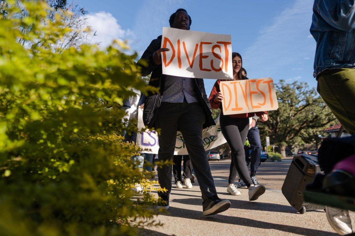 Demonstrators carry signs reading &#8220;Divest&#8221; on Friday, Nov. 18, 2022, on South Stadium Drive in Baton Rouge, La.