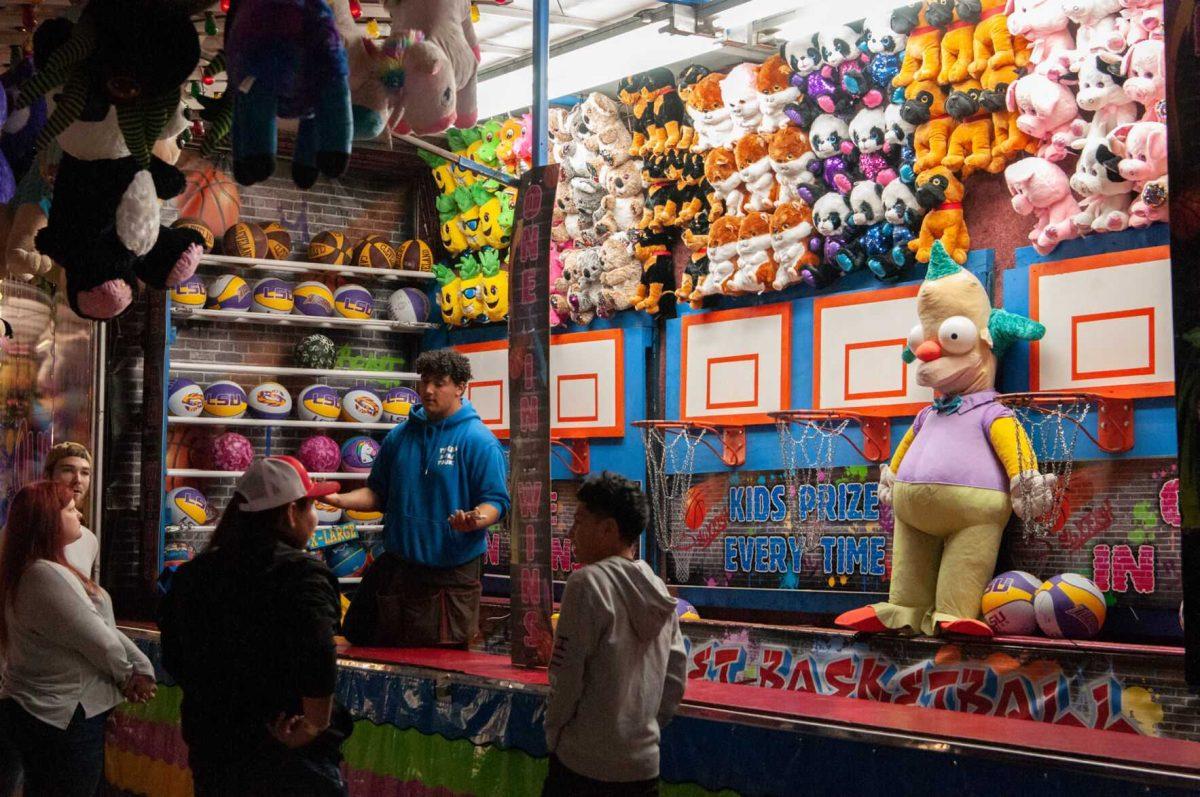 A family approaches a basketball game station while a stuffed Krusty the Clown watches at the Greater Baton Rouge State Fair on Sunday, Oct. 30, 2022, at the Lamar Dixon Expo Center in Gonzales, La.