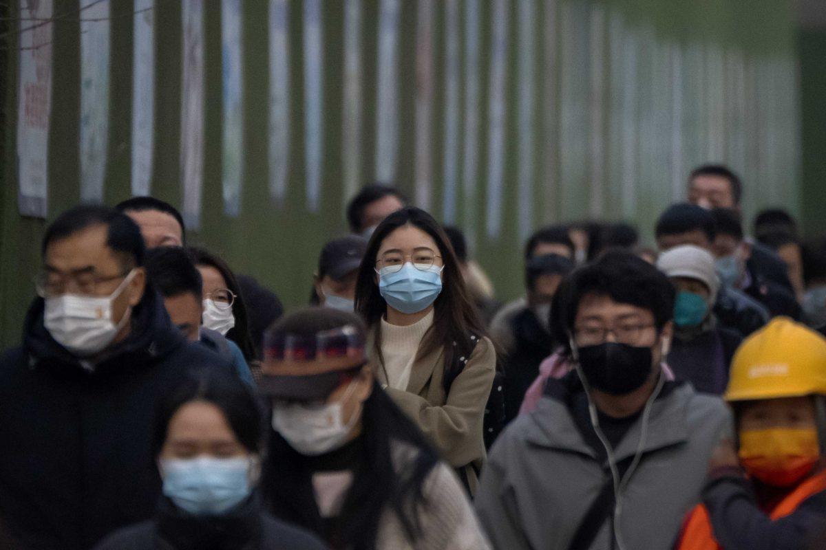 Commuters wearing face masks walk along a street during the evening rush hour in the central business district in Beijing, Friday, March 17, 2023. (AP Photo/Mark Schiefelbein)