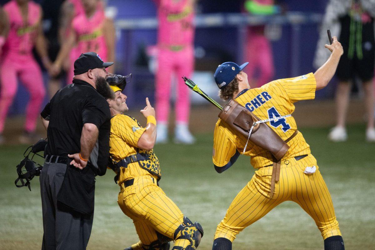 Savannah Bananas pitcher Andy Archer (24) takes a selfie with an umpire and catcher Bill Leroy (1) mid-game Thursday, March 14, 2024, during the Savannah Bananas 5-4 loss to the Party Animals during their world tour stop at Alex Box Stadium in Baton Rouge, La.