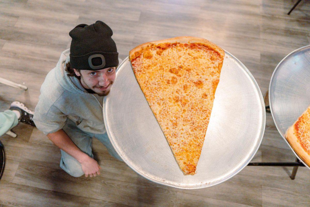 Jacob Chastant kneels next to his humungous slice of pizza Sunday, Feb. 18, 2024, at Fat Boy's Pizza on Nicholson Drive in Baton Rouge, La.