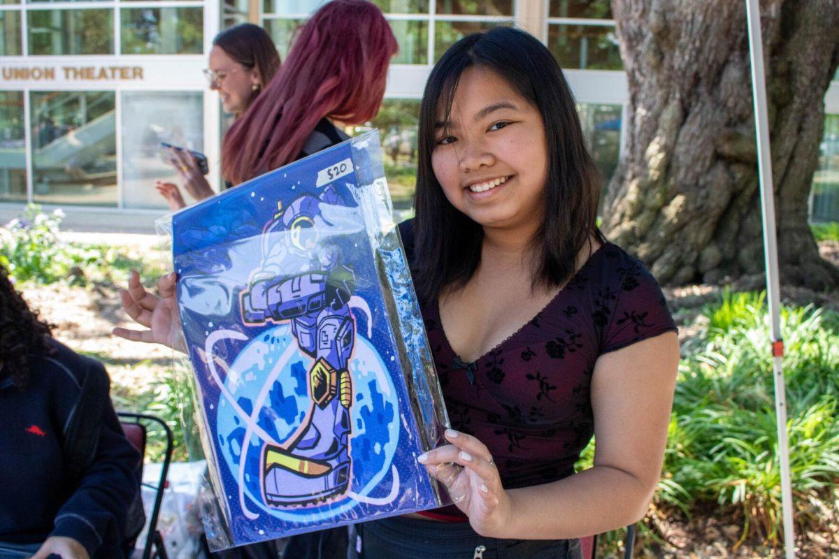 A student poses with her poster sized print she made at the art sale on Wednesday, April 24, 2024, in Free Speech Alley on LSU's campus.