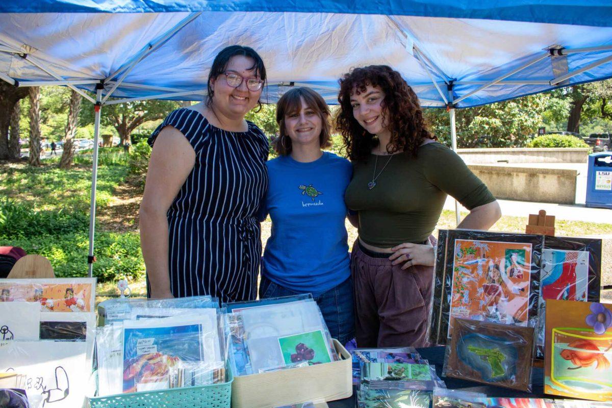 Three students pose with their work at the art sale on Wednesday, April 24, 2024, in Free Speech Alley on LSU's campus.