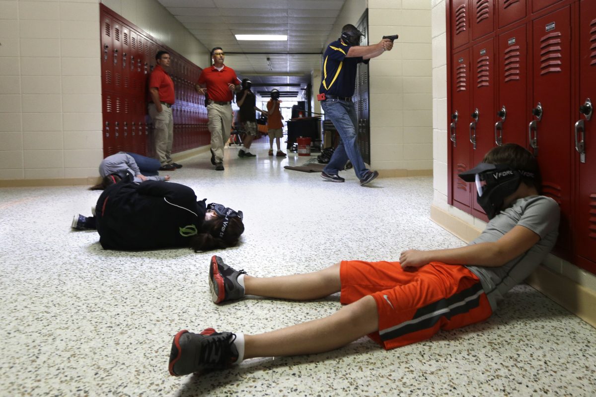 FILE - In this file photo taken July 11, 2013, a Clarksville Schools faculty member, top right, carries an air-powered practice handgun to a classroom as firearms instructors, left, watch and students, lying on the floor, portray victims during a training exercise in Clarksville, Ark. Arkansas' attorney general on Thursday, Aug. 1 said in an opinion issued by his office that the Arkansas board of Private Investigators and Private Security Agencies doesn't have the authority to license school districts to employ teachers and staff as armed guards.