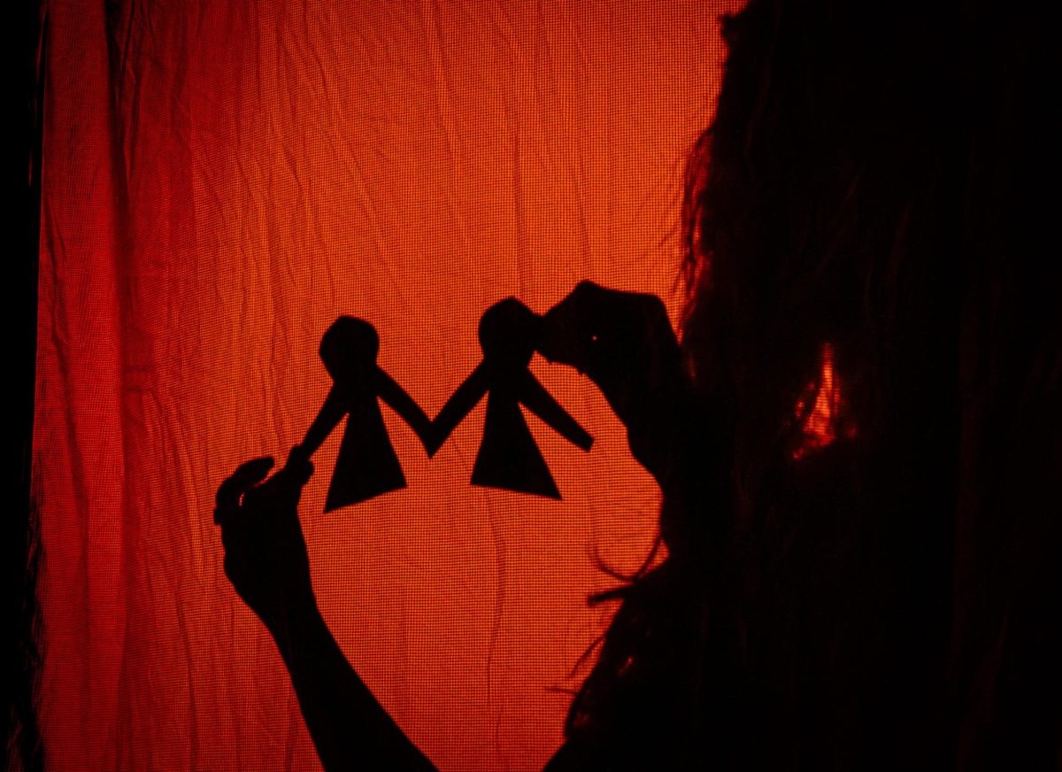 A silhouette holding paper figures in Hopkins Black Box Theatre's "Small White Star." 