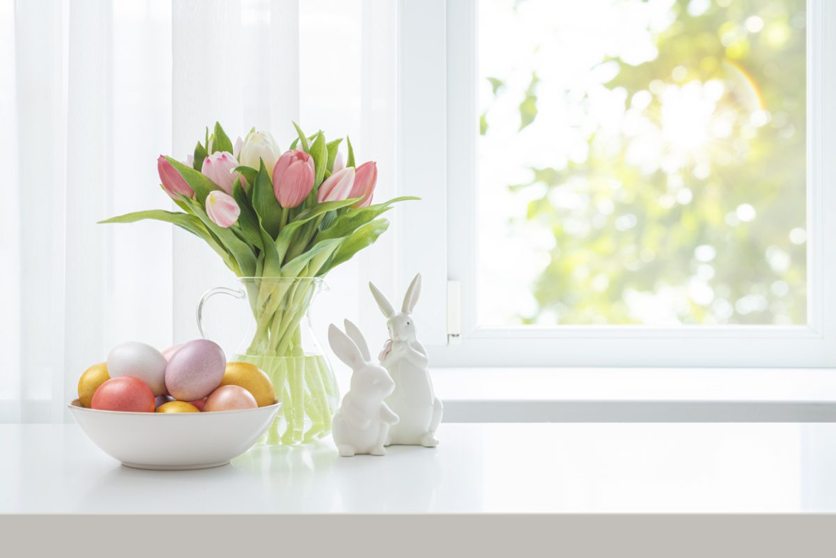 Easter eggs in bowl, fresh tulip flowers and ceramic bunny rabbits on blur spring window background